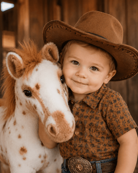 Child in cowboy hat with a toy horse in front of a wooden barn.