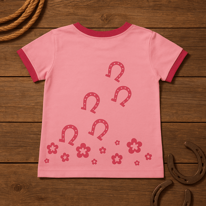 Pink horse t-shirt with horseshoe designs on a wooden surface