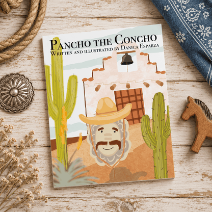 A children's book titled 'Pancho the Concho' by Danica Esparza is displayed on a rustic white-washed wooden surface. The book cover features a colorful illustration of a cowboy with a mustache, a white adobe building, and green cacti.
