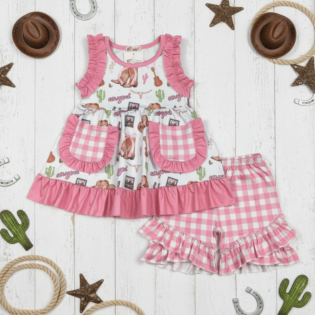Children's pink and white short set with ruffles on a wooden background with cowboy-themed decorations.