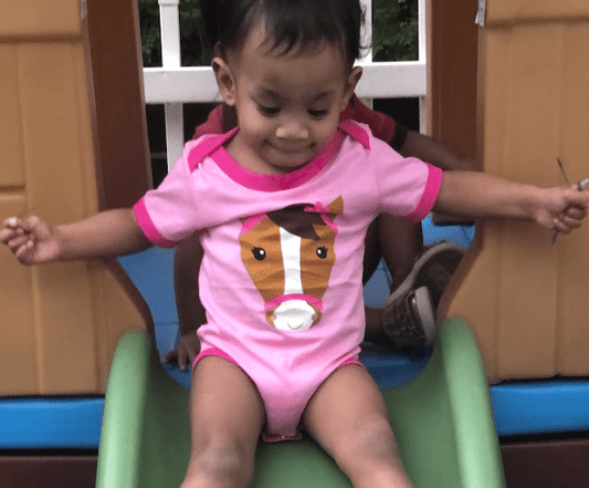 Child in a pink romper with a horse design on a slide
