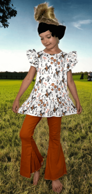 Young girl in a floral top and orange bell-bottom pants standing in a grassy field.