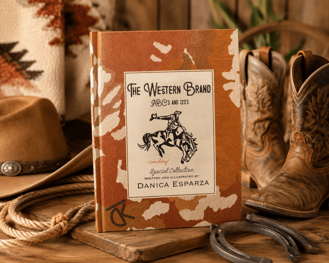 A Western-themed hardcover book titled 'The Western Brand' stands upright on a wooden surface, surrounded by cowboy boots, a hat, rope, horseshoes, and a blanket in a rustic styled setting.