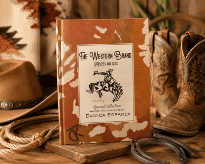 A Western-themed hardcover book titled 'The Western Brand' stands upright on a wooden surface, surrounded by cowboy boots, a hat, rope, horseshoes, and a blanket in a rustic styled setting.