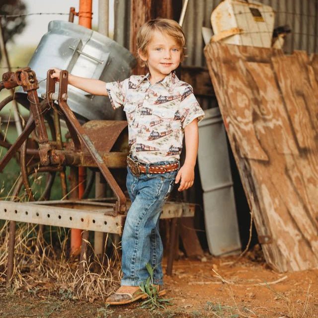 Young cowboy standing outdoors near rustic farm equipment