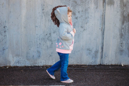 Child wearing a gray hoodie with horseshoe designs and blue jeans walking against a textured wall.