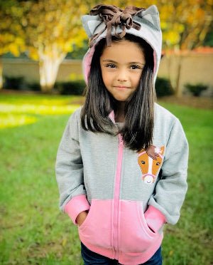Child wearing a gray and pink hoodie with horse ears outdoors