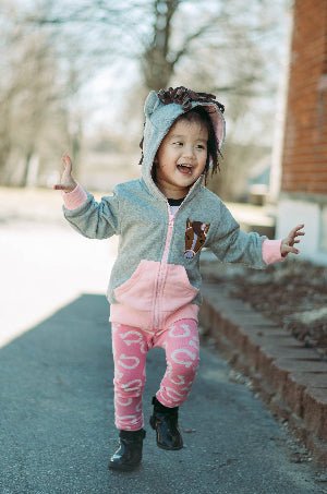 Child wearing a pink and gray outfit with horse ears, standing on a sidewalk.
