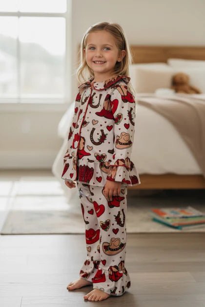 Child wearing pajamas with cowboy and heart patterns in a bedroom.