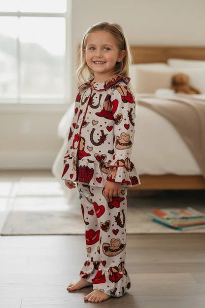 Child wearing pajamas with cowboy and heart patterns in a bedroom.