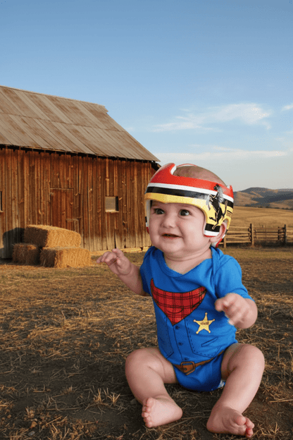 Baby in a sheriff romper with a helmet sitting in a barnyard