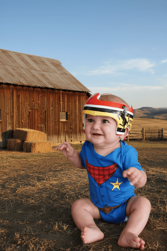 Baby in a sheriff romper with a helmet sitting in a barnyard