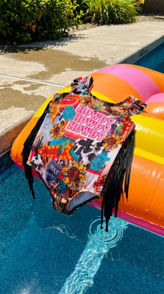 Colorful swimsuit with 'Howdy' text and graphics on a pool float by a pool.