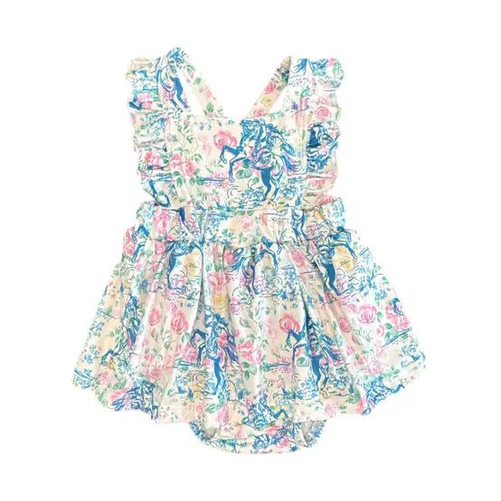 A sleeveless baby romper dress with a colorful floral and toile-style print on a cream background, featuring ruffled shoulder straps and a gathered flared skirt.