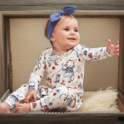 Baby girl in Annie Oakley western romper sitting on bench