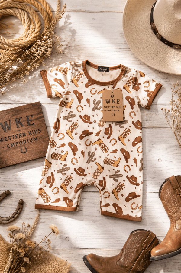 Baby romper with western pattern on a wooden surface with cowboy boots and hat.