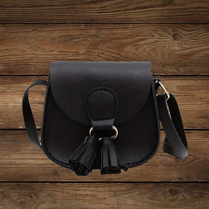 Black mini crossbody purse with tassel detail on wood background.