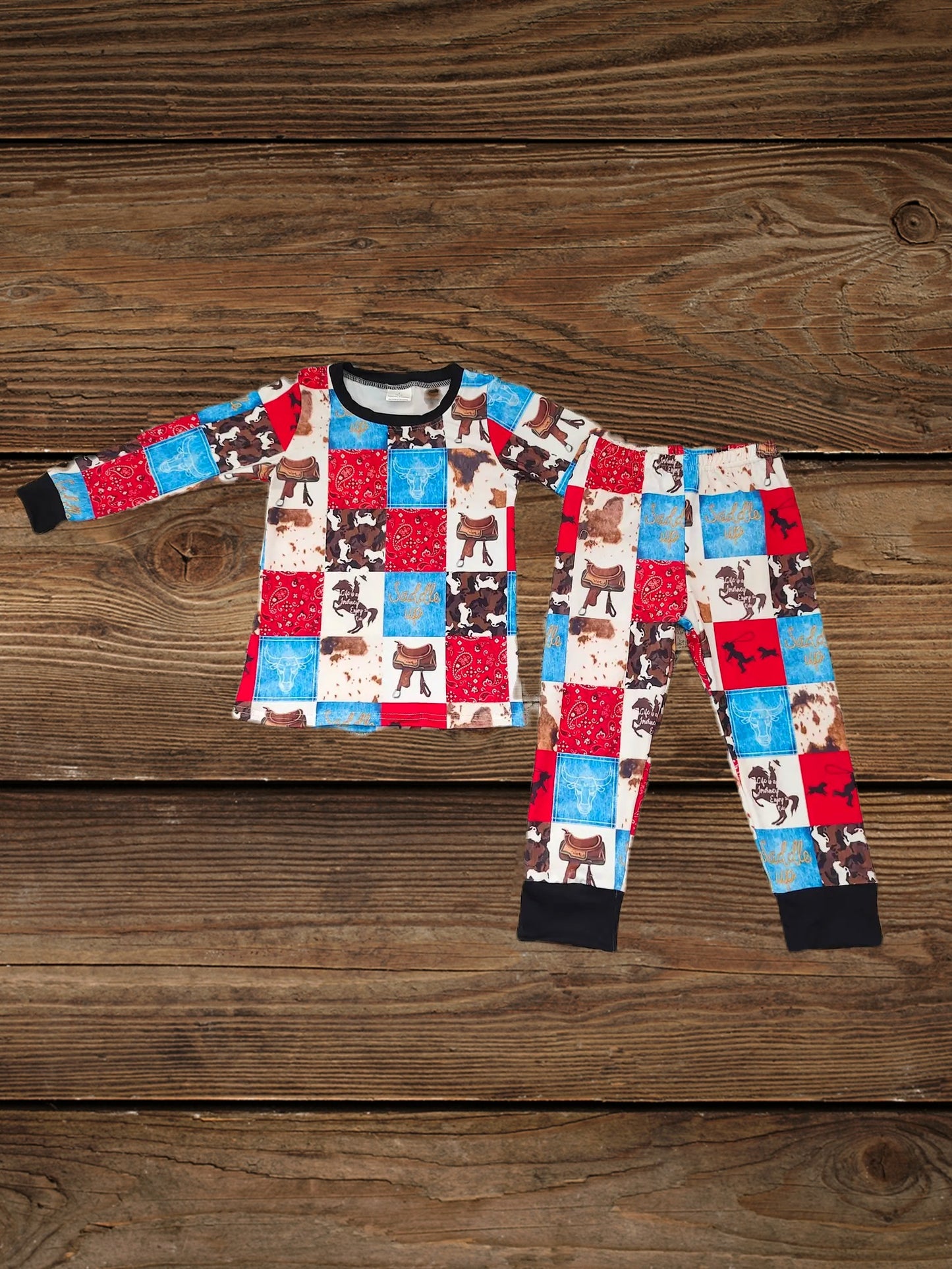 Folded cowboy pajamas kids set with horse print and western bandana patches, warm long-sleeve kids pajama set displayed on wooden background