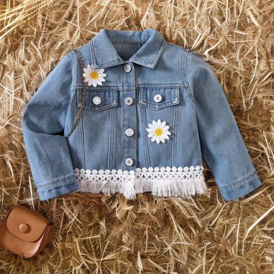 Toddler western denim jacket with daisy patches and fringe hem displayed on straw background.