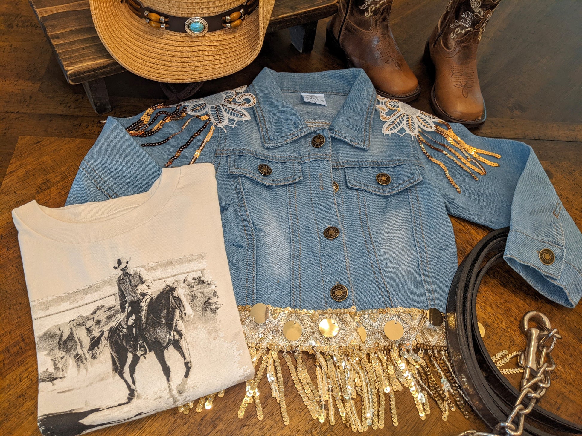 Western-themed flat lay featuring Glitter & Glamour Girls' Sequin Tassel Denim Jacket with fringe, hat, boots, and tee.