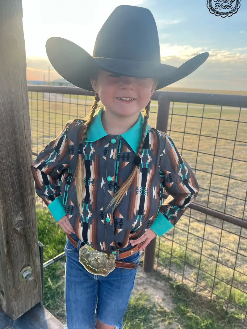 Side view of young cowgirl wearing Aztec Western shirt and cowboy hat in ranch setting