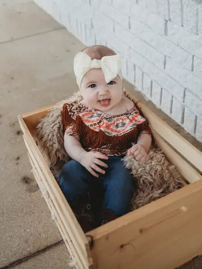 Toddler girl wearing off-shoulder Aztec onesie sitting in a wooden crate