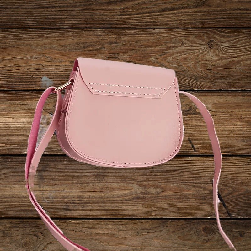 Back view of pink mini crossbody purse with adjustable strap on wood background.