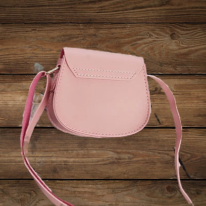 Back view of pink mini crossbody purse with adjustable strap on wood background.