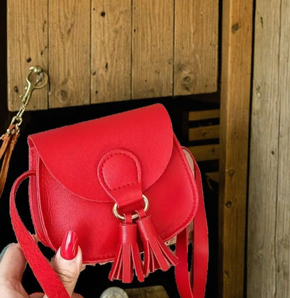 Red mini crossbody purse with tassel held in hand, Western-inspired.