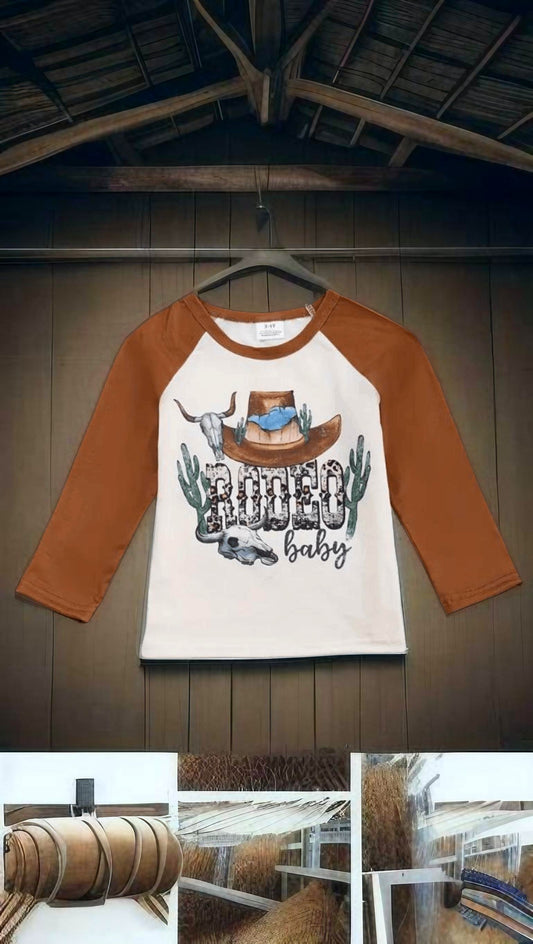 Long sleeve baby bodysuit with red rodeo print hanging on barn wall