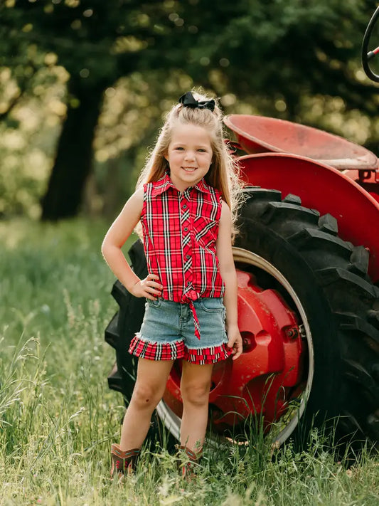 Girl in ruffled denim cowgirl shorts standing beside red tractor