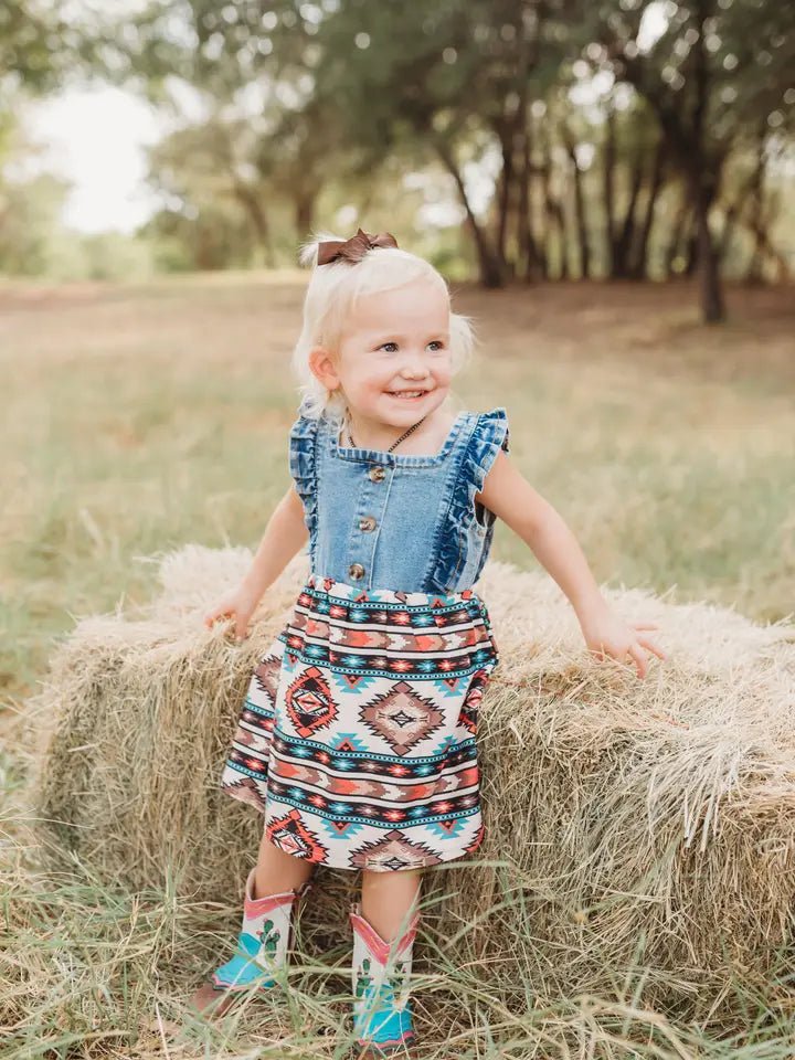 Toddler girl in Aztec dress standing on hay in field