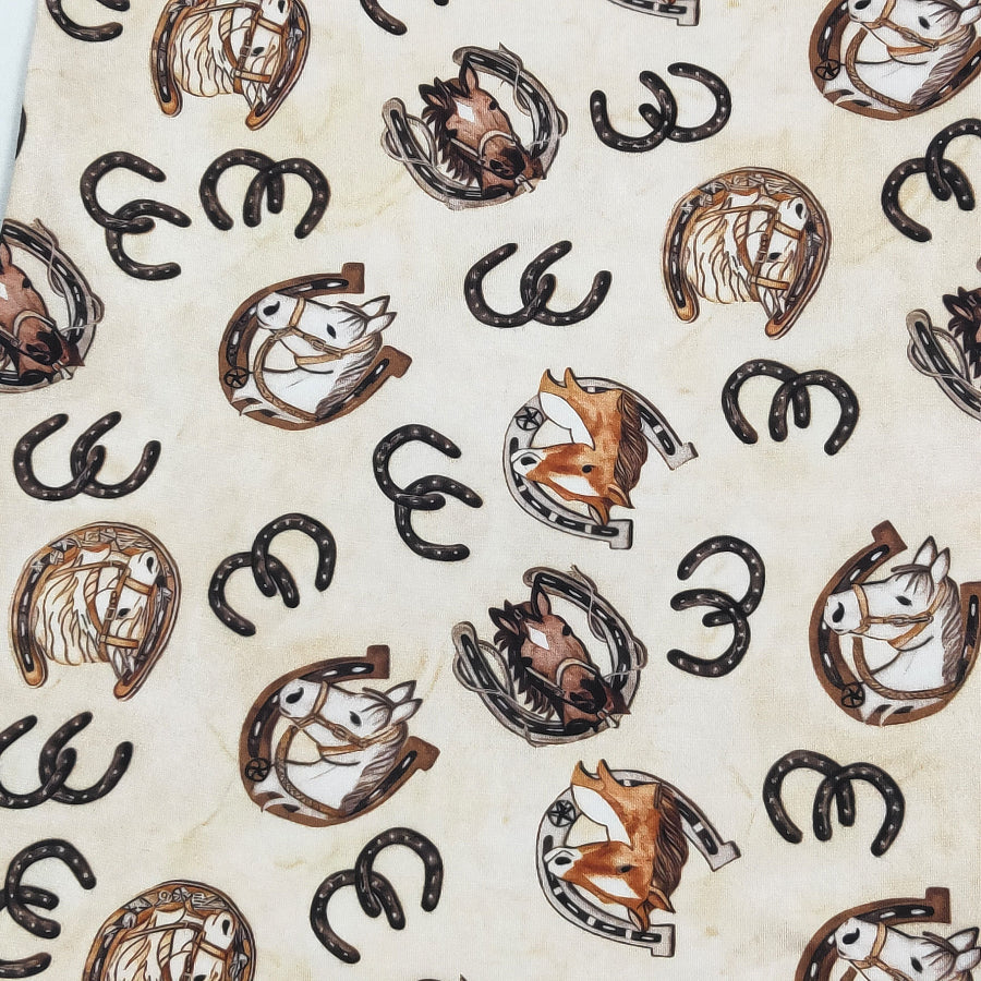 A close-up of a fabric or material print featuring repeating illustrations of horseshoes, horses, and foxes in brown, black, and white on a warm cream background.